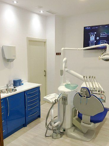 Sala de examen dental con gabinetes azules, sillón dental y equipo.