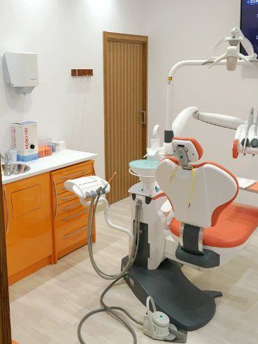 Interior de consultorio dental con gabinetes de color naranja, una silla dental y una puerta marrón cerrada.