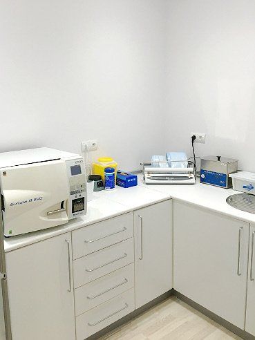 Sala de esterilización en un consultorio dental con esterilizador, lavabo y armarios; paredes blancas.