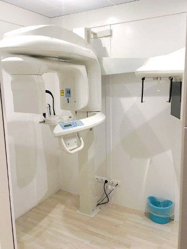 Una máquina de rayos X panorámicos dentales en una sala blanca. Un cubo de basura azul a un lado.