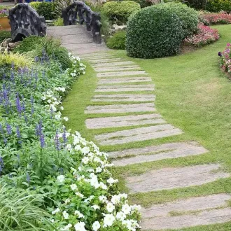 Un camino de piedra que conduce a un puente en un jardín rodeado de flores.