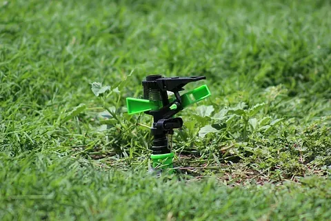 Un aspersor verde y negro se encuentra sobre un exuberante césped verde.
