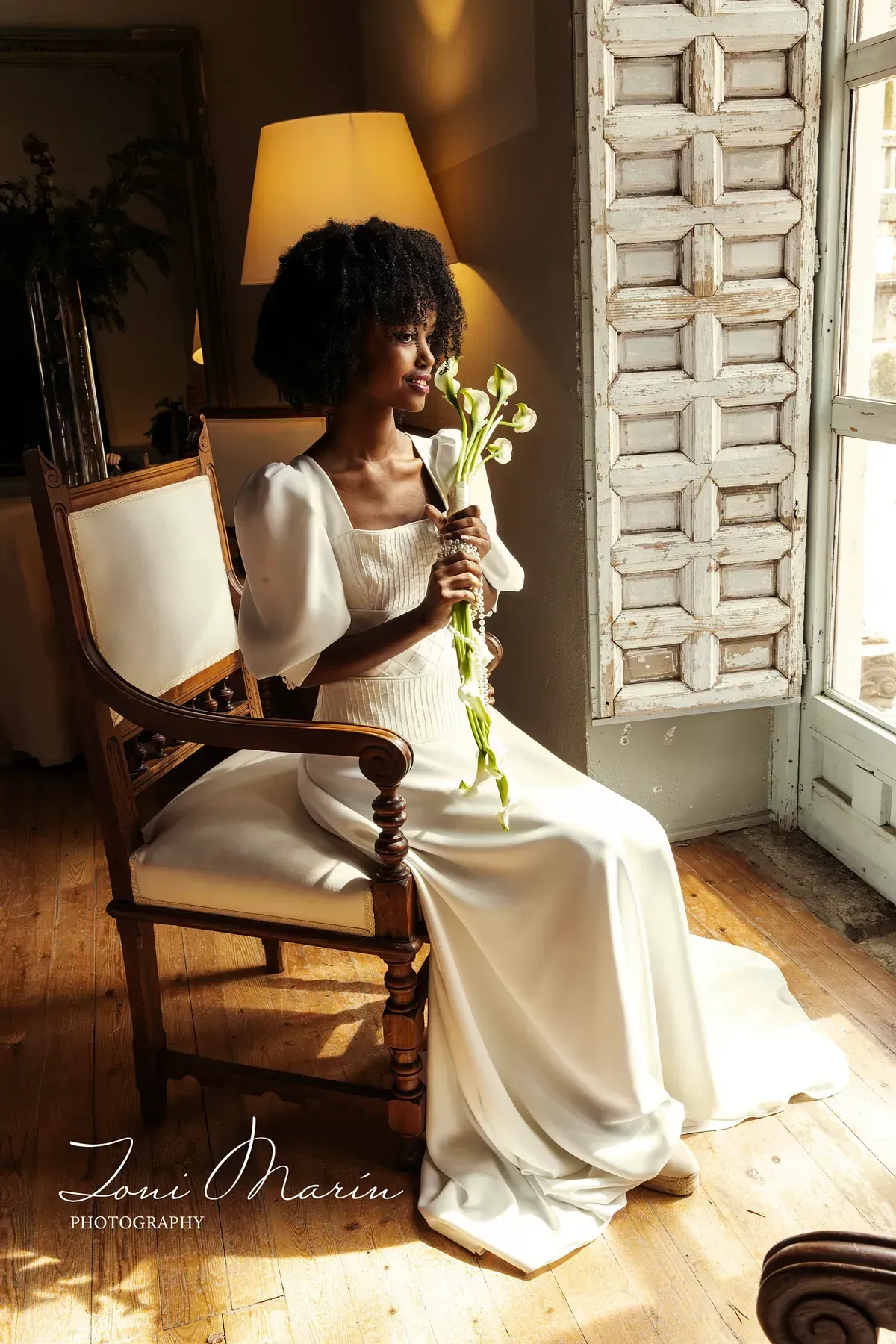 Una mujer con un vestido de novia está sentada en una silla sosteniendo un ramo de flores.