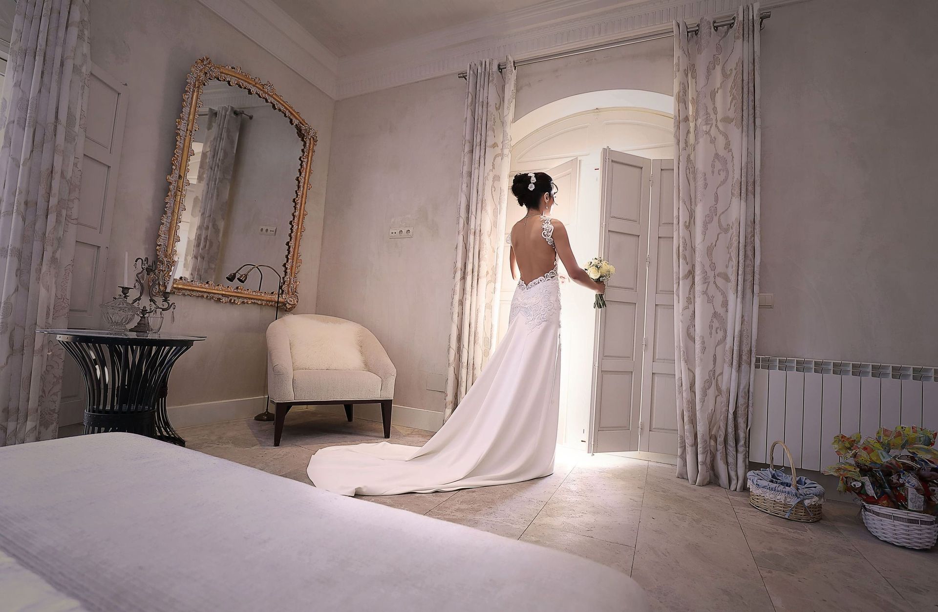 Una novia con un vestido de novia está de pie en un dormitorio sosteniendo un ramo de flores.
