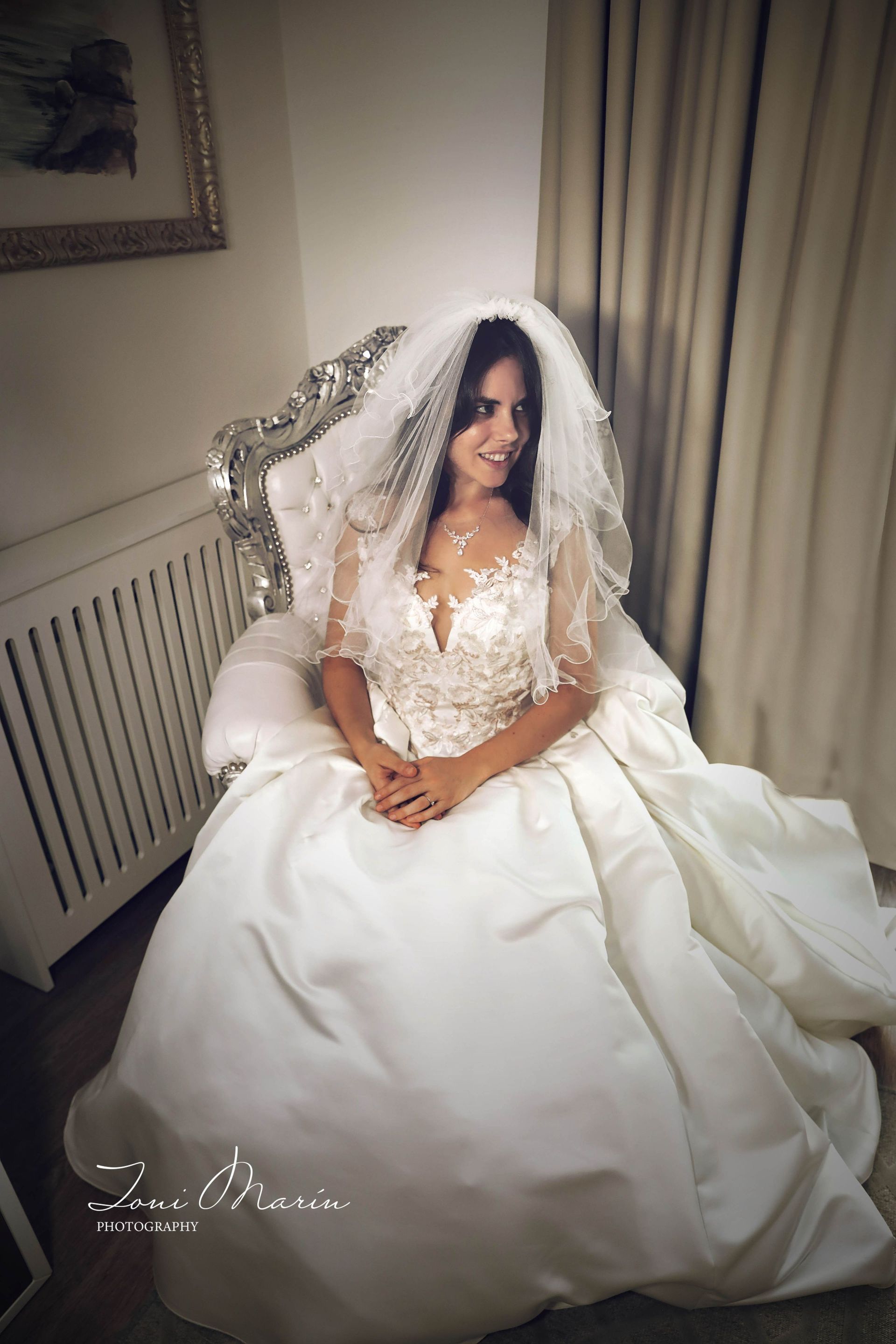 Una mujer con un vestido de novia y velo está sentada en una silla.