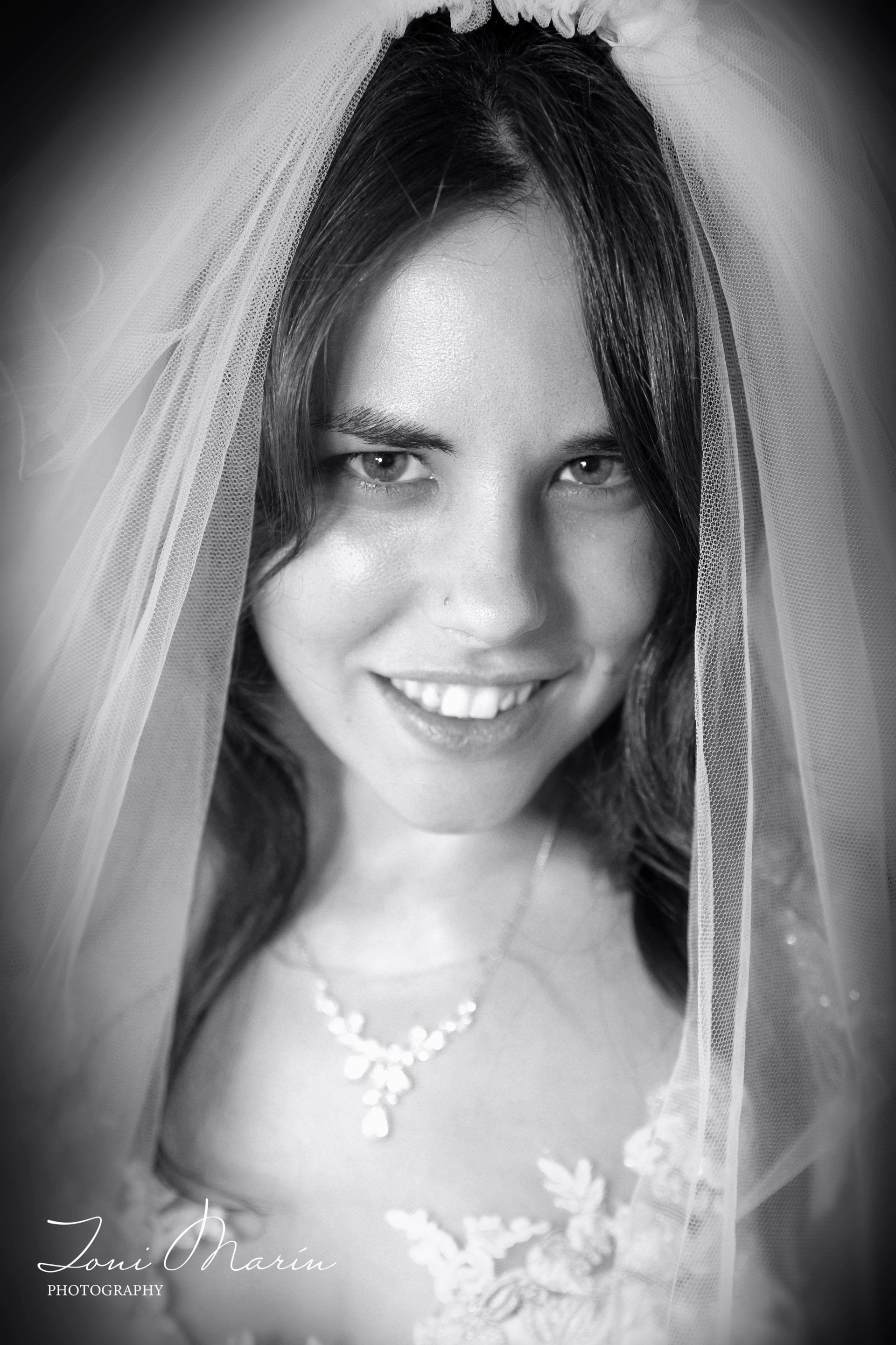 Una mujer con un vestido de novia y velo sonríe en una foto en blanco y negro.