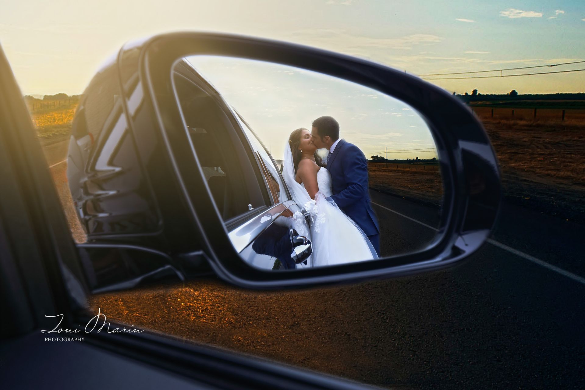 Una novia y un novio se besan en el espejo retrovisor de un coche.