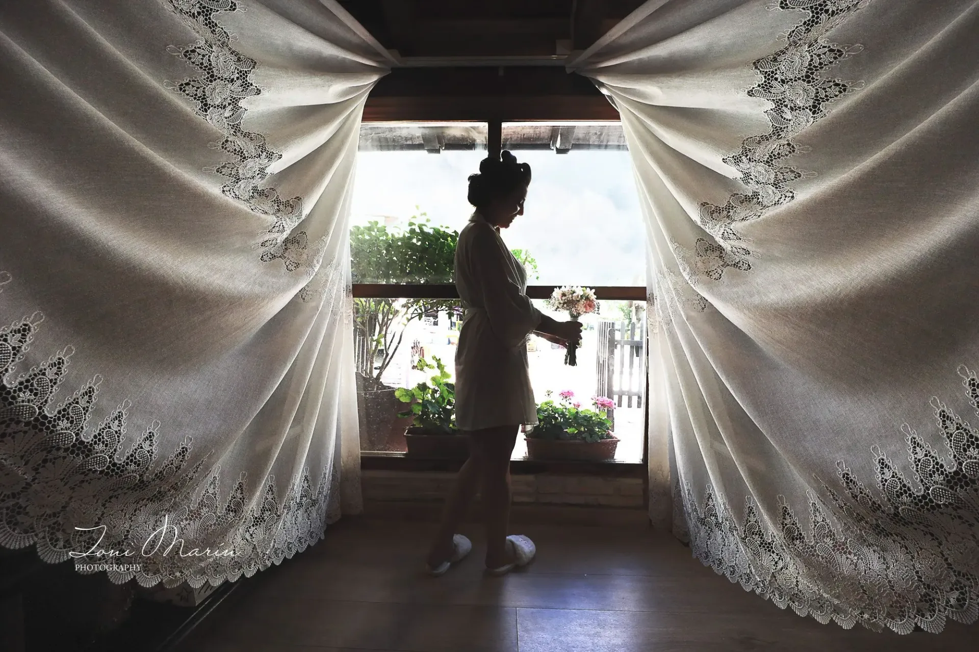 Una mujer está parada frente a una ventana sosteniendo un ramo de flores.