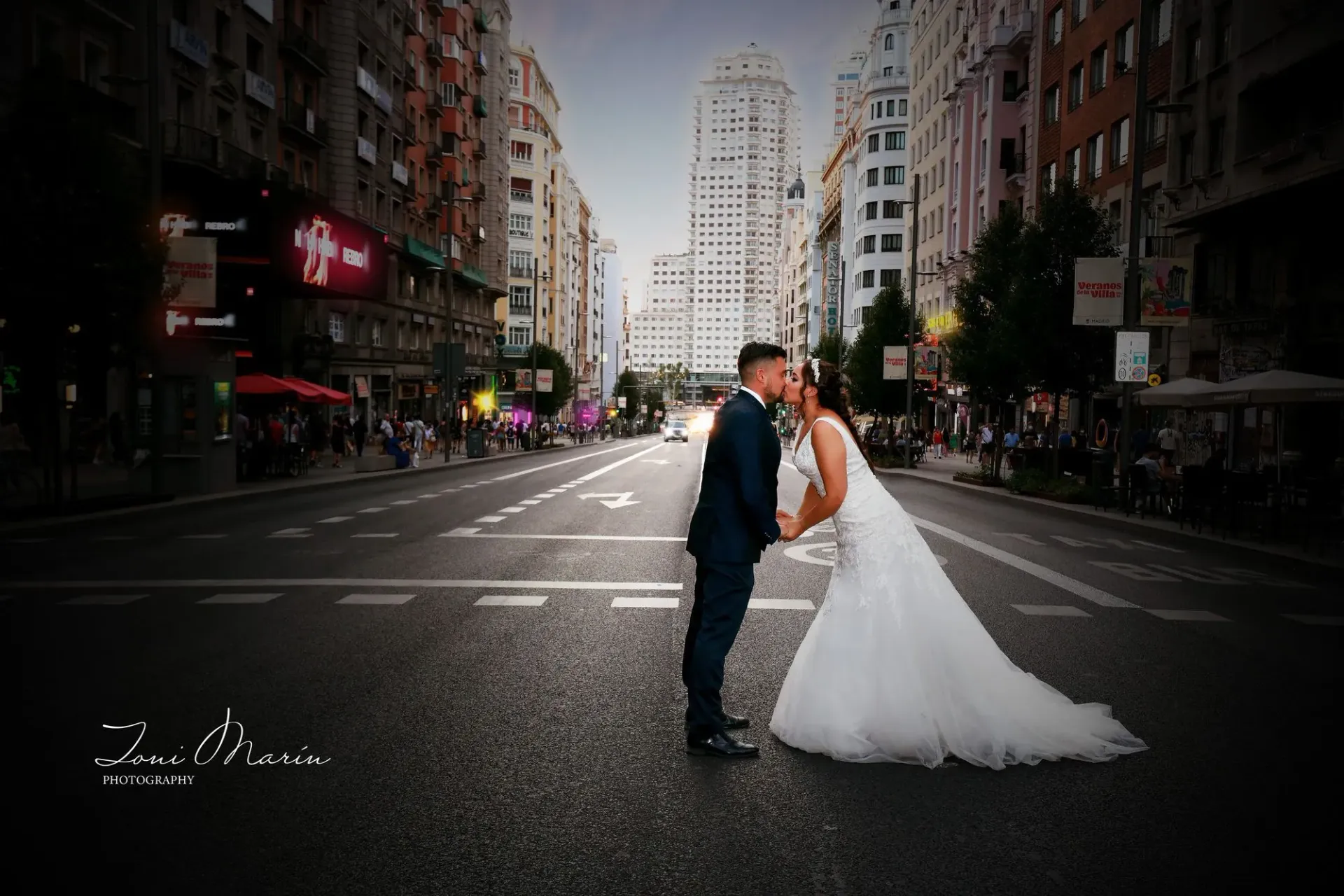 Una novia y un novio se besan en medio de una calle de la ciudad.