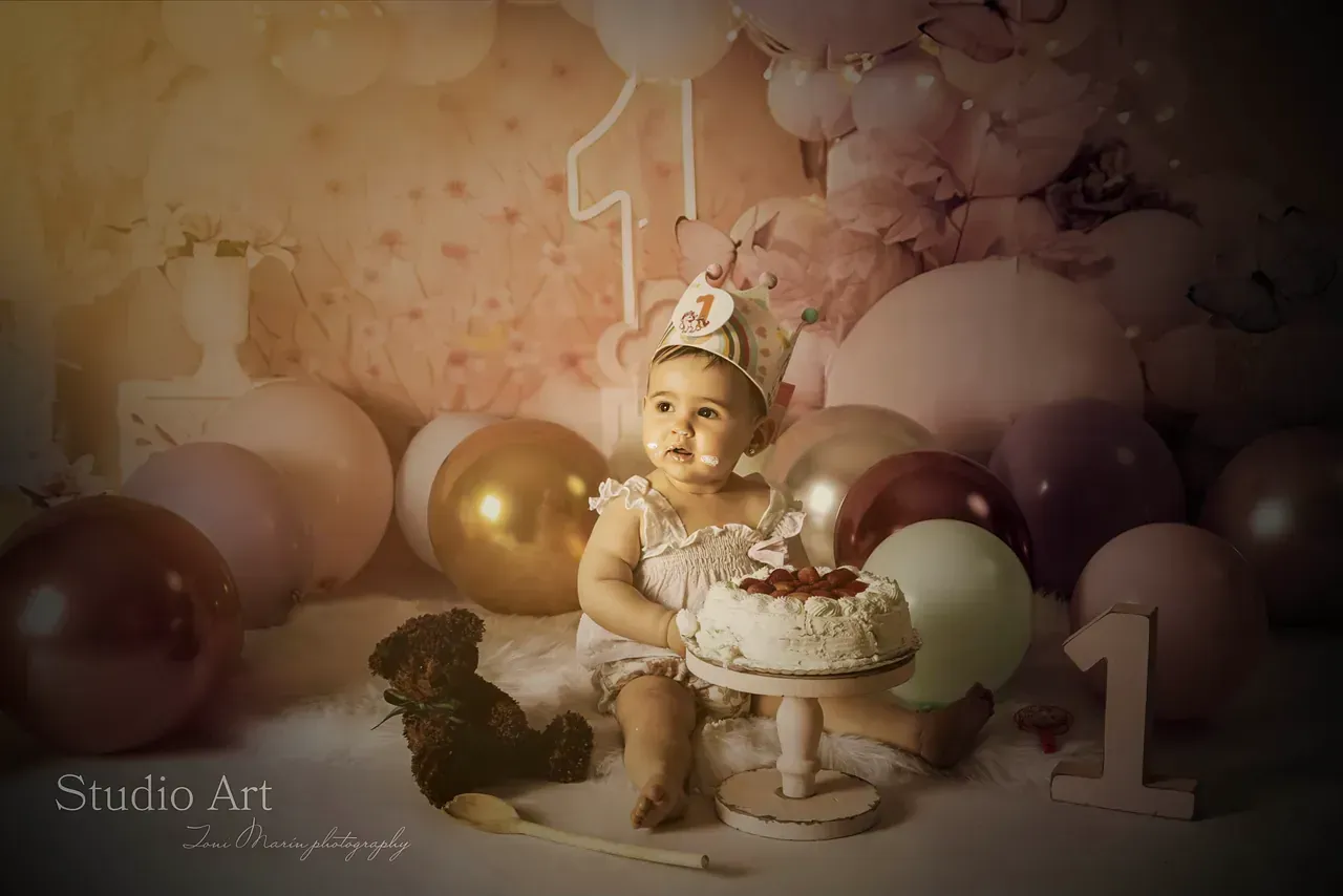 Una niña está sentada junto a un pastel y globos.