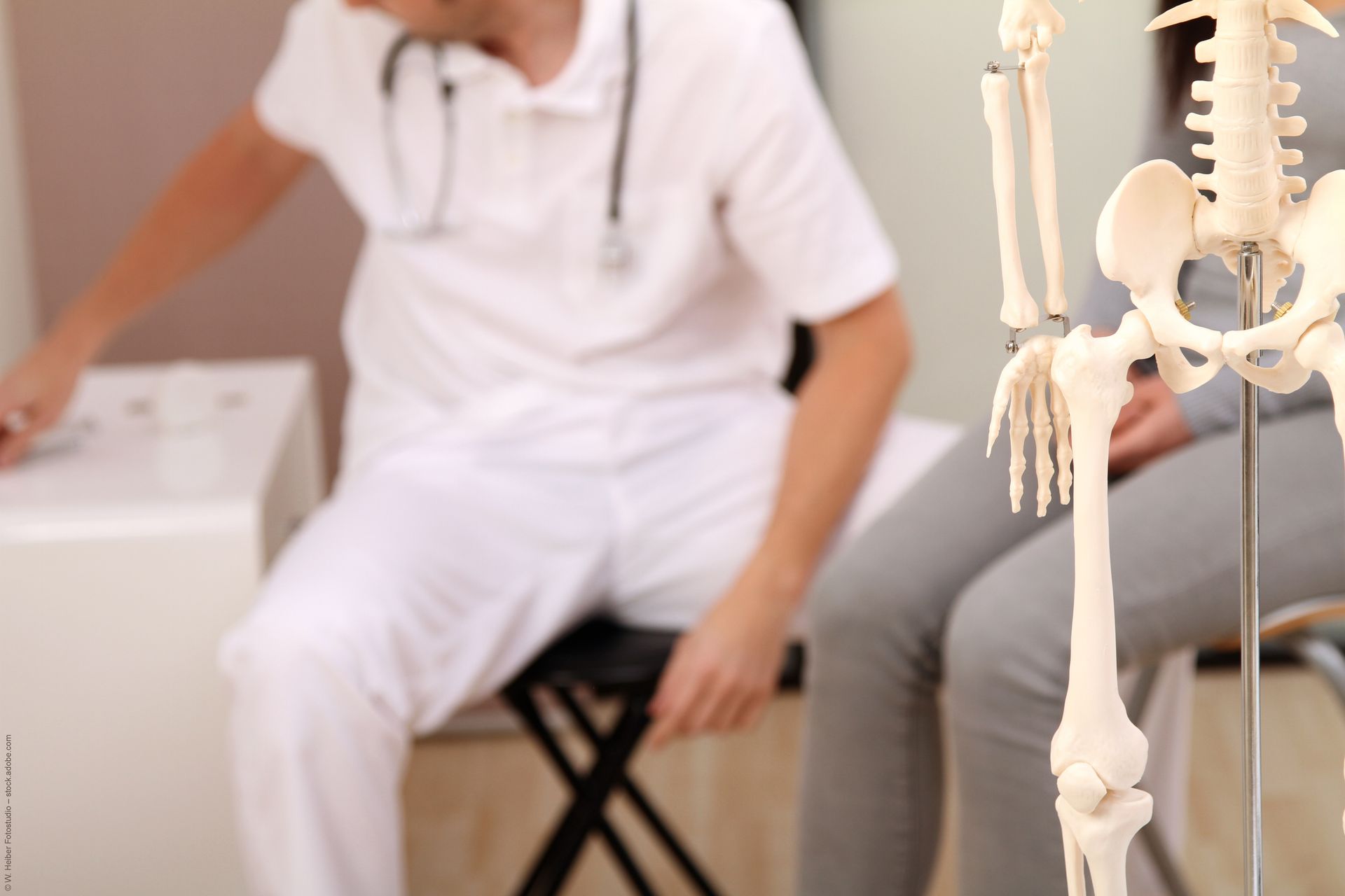 Orthopäde in einer Beratung mit einem Patienten und daneben steht ein Skelett-Modell