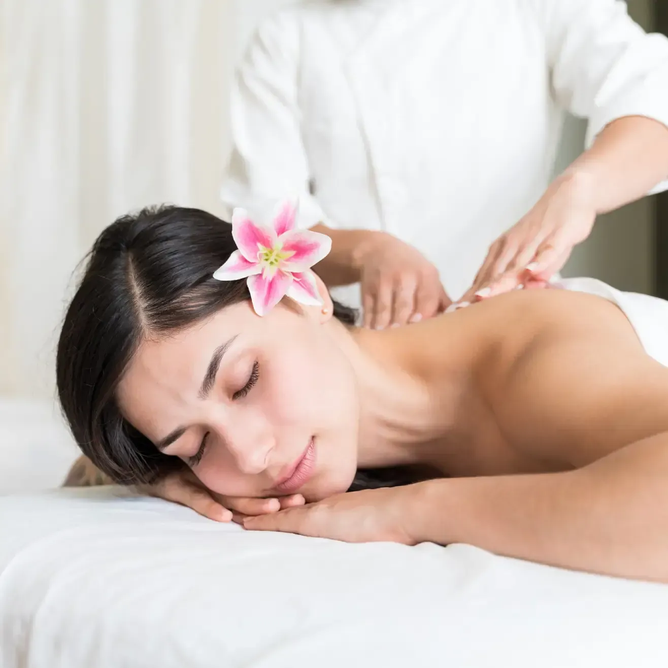 Una persona con un lirio en el pelo recibe un relajante masaje de espalda mientras está tumbada en una camilla blanca.