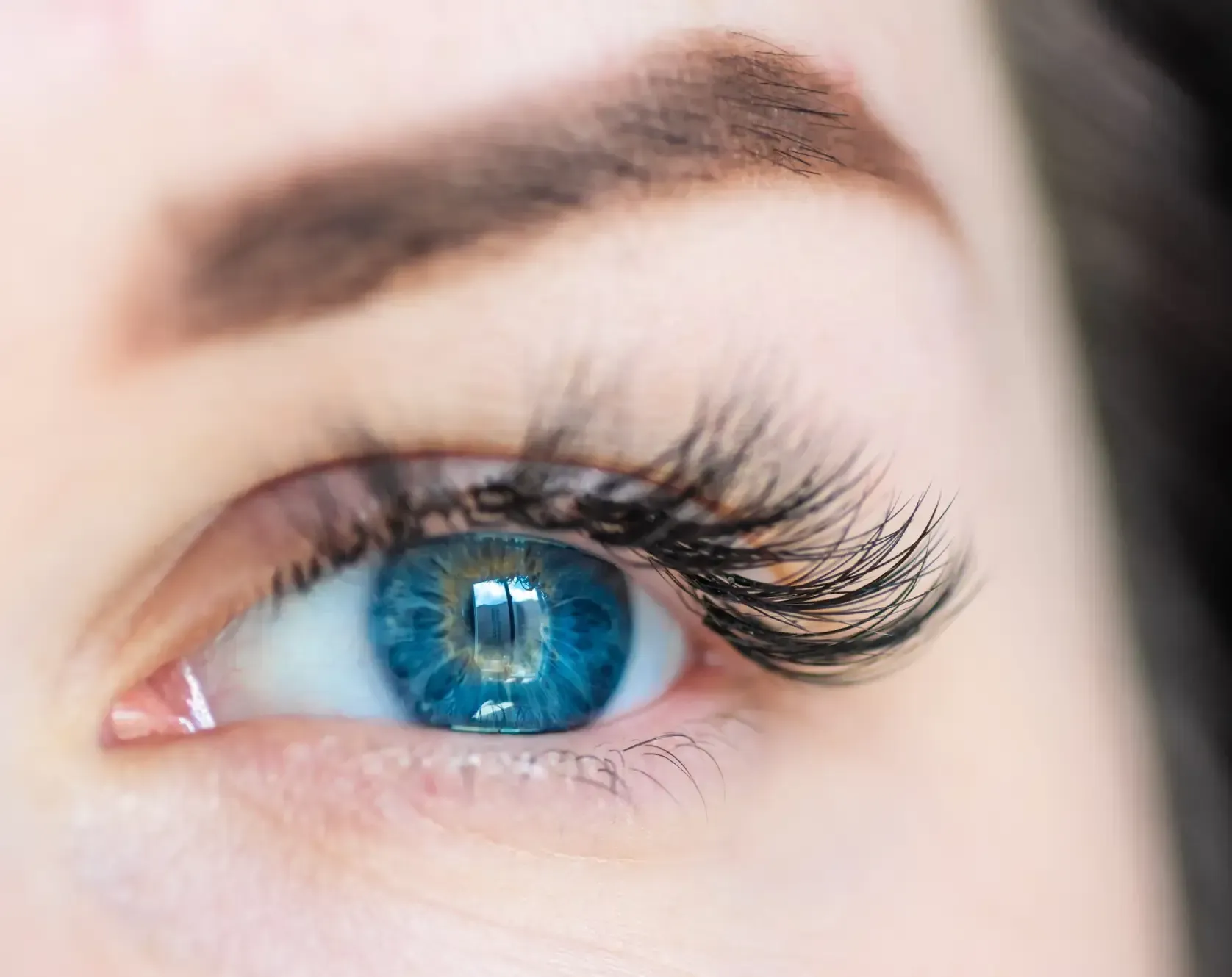 Primer plano de un ojo humano con iris azul vibrante, pestañas oscuras y bien definidas, y una ceja rellena.