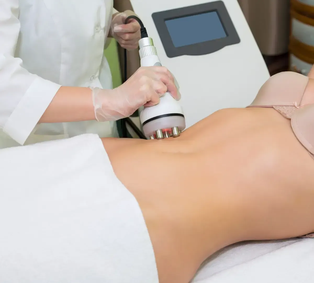 Un profesional con bata blanca utiliza un dispositivo cosmético manual en el abdomen de una persona durante un tratamiento de remodelación corporal.