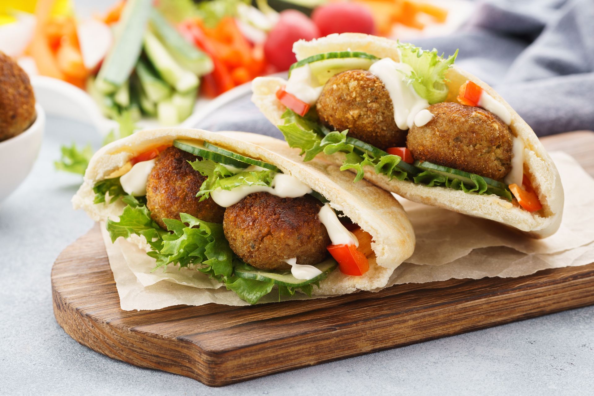 Mit Falafel gefüllte Pita-Taschen mit Gemüse und weisser Sosse, serviert auf einem Holzbrett.