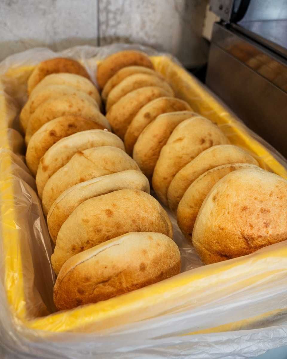 Goldbraun gebackene Käsebrötchen in einem gelben, rechteckigen, mit Plastik ausgekleideten Behälter.