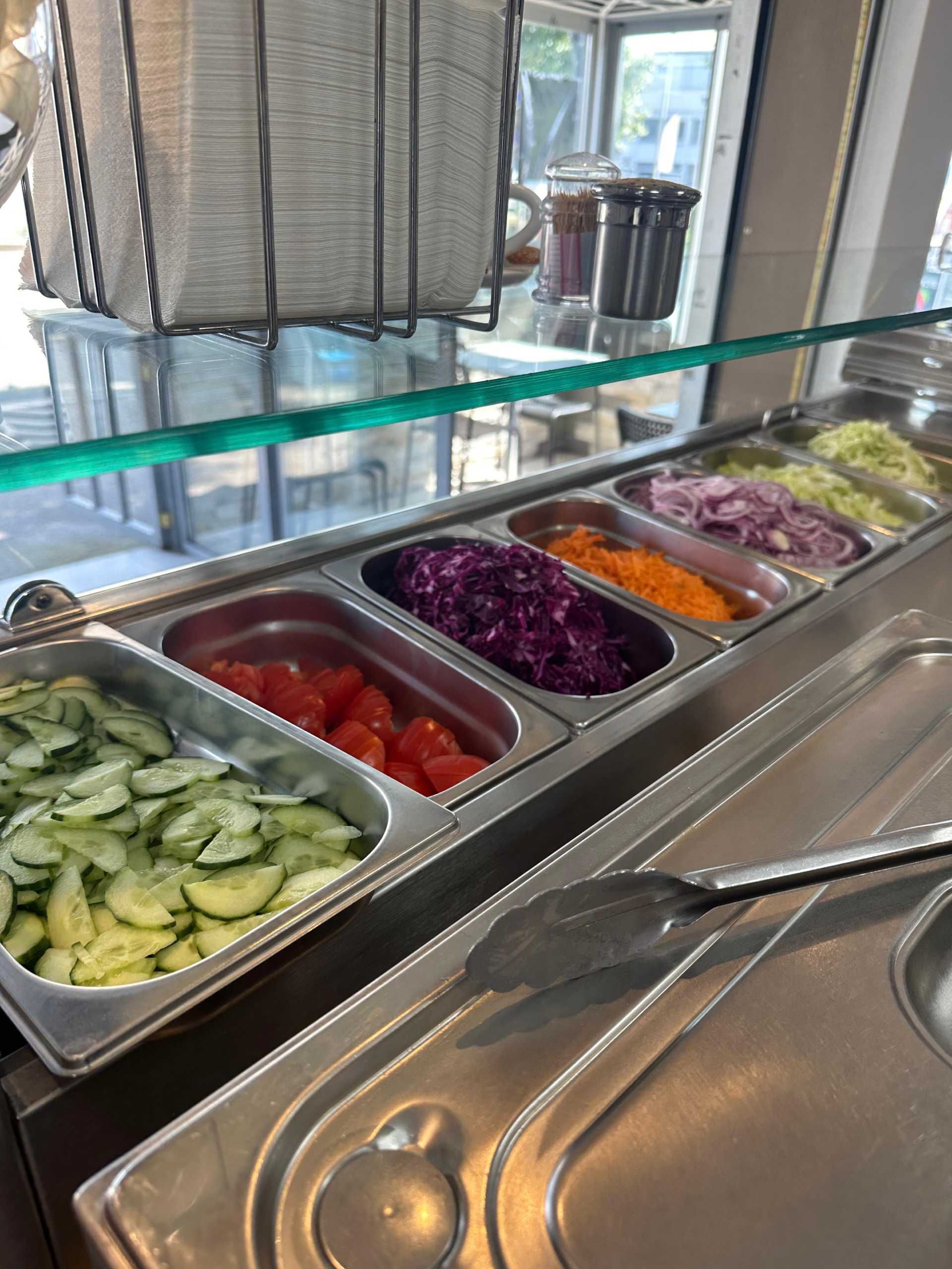 Salatbar mit geschnittenen Gurken, Tomaten, rotem und orangefarbenem Gemüse sowie gehobeltem Kohl.