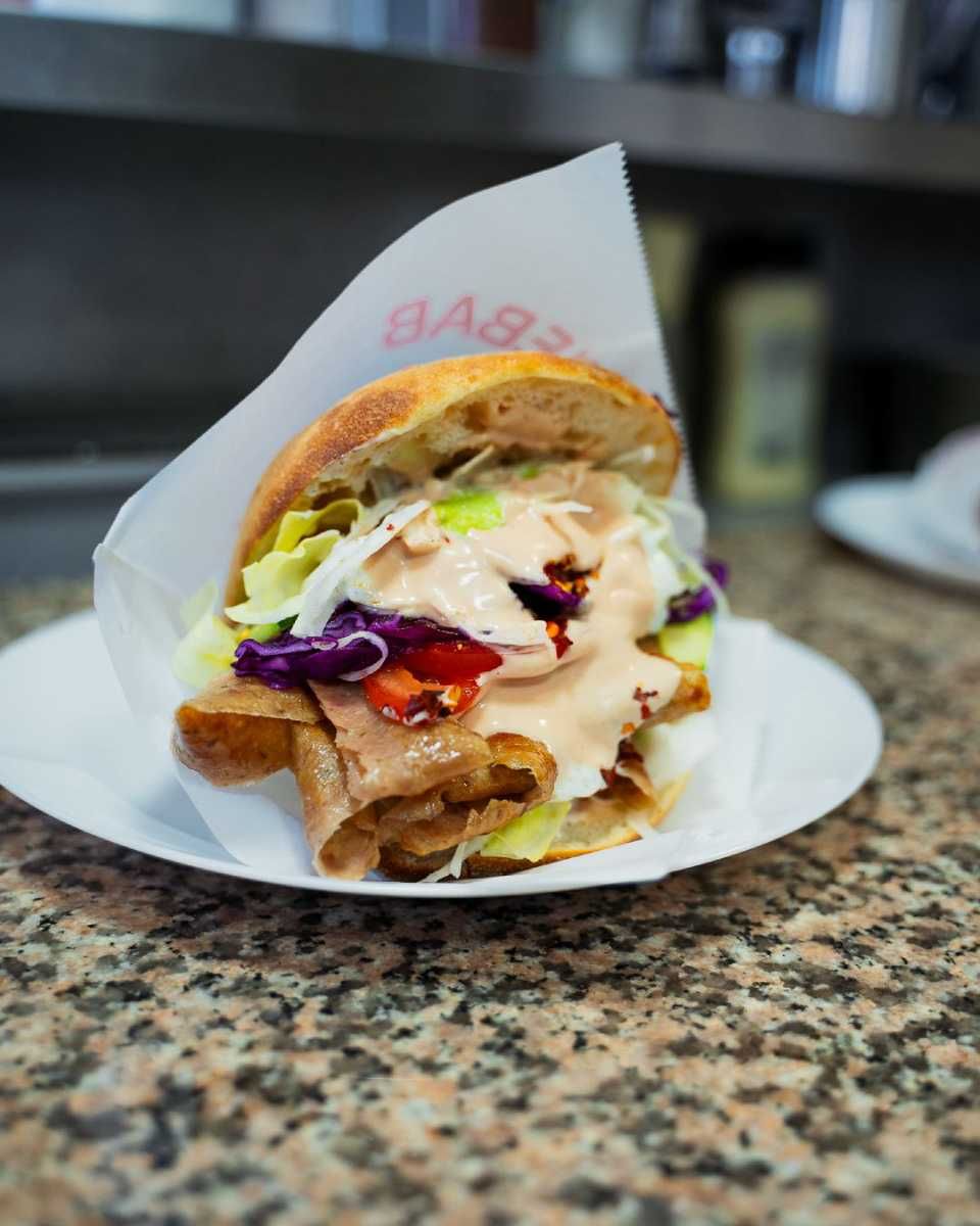 Döner Kebab in weissem Papier auf einem weissen Teller, gefüllt mit Fleisch, Gemüse und Sosse, auf einer Granittheke.