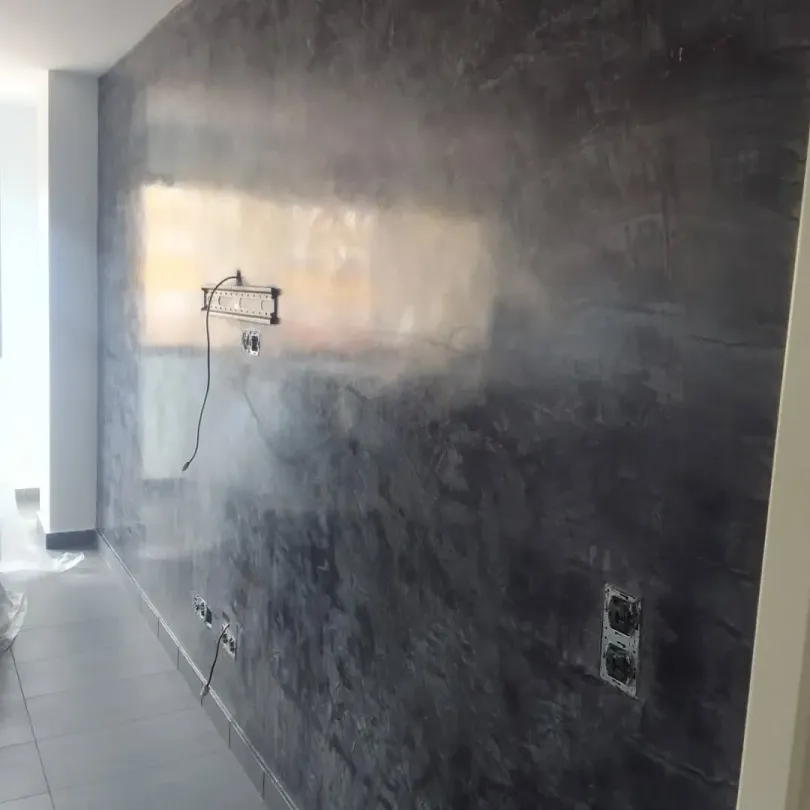 Pared grisácea con vetas de luz, enchufes y una lámpara. Interior.