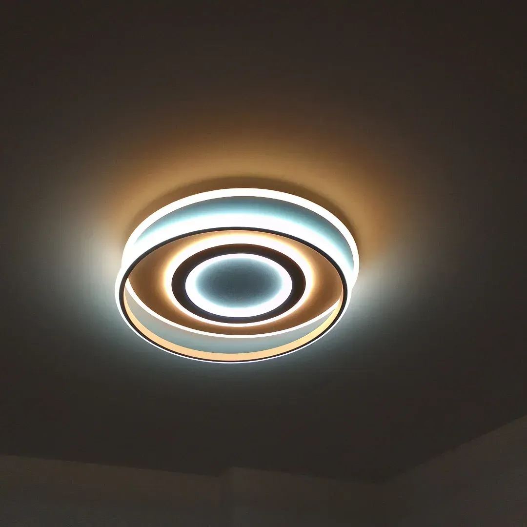 Luminaria de techo circular con múltiples anillos, que emite una suave luz blanca y cálida amarilla.