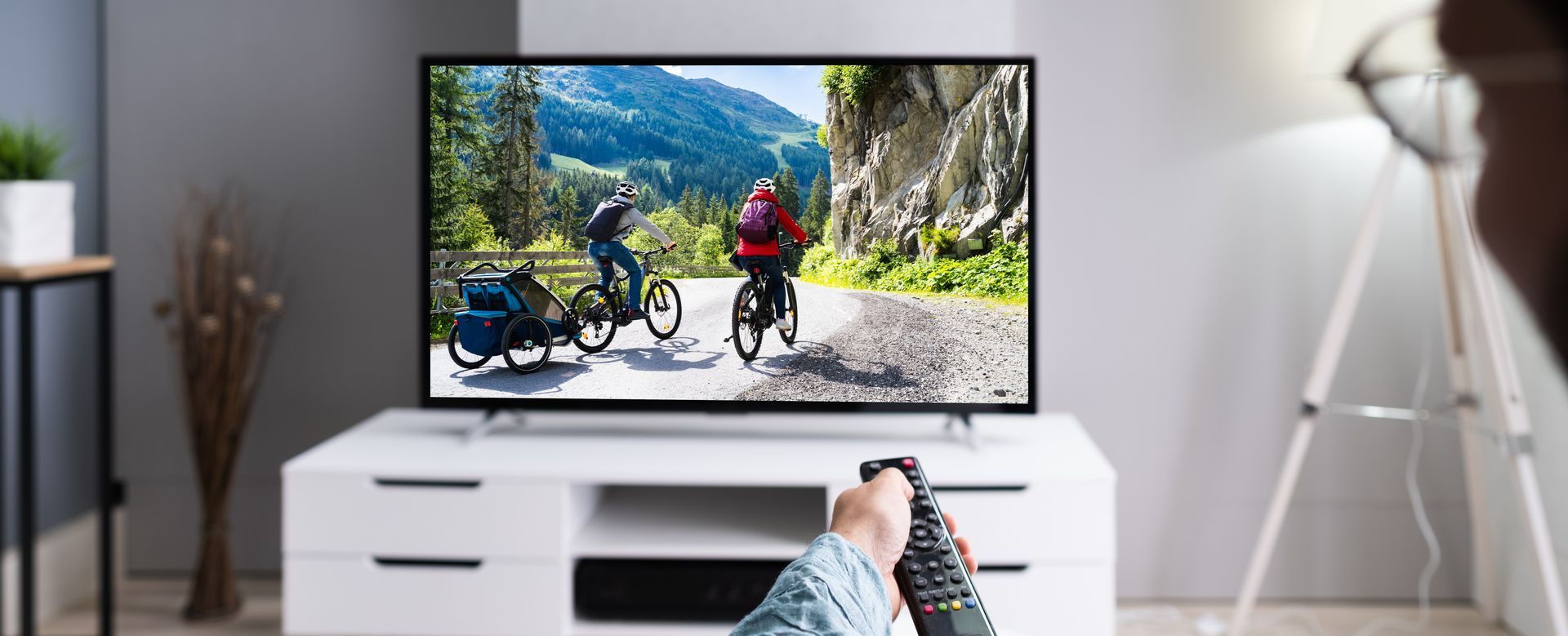 Télévision du salon montrant des cyclistes sur une route de montagne, regardée depuis le canapé, télécommande en main