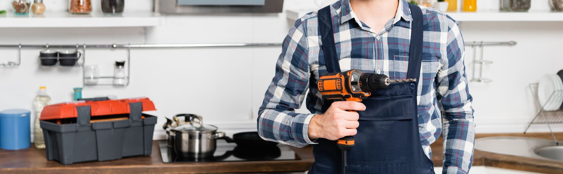 Une personne en chemise à carreaux tient une perceuse sans fil dans un atelier de cuisine.