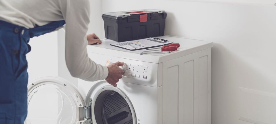 Une personne ajuste un appareil électroménager blanc, avec des outils dessus, dans une pièce lumineuse.