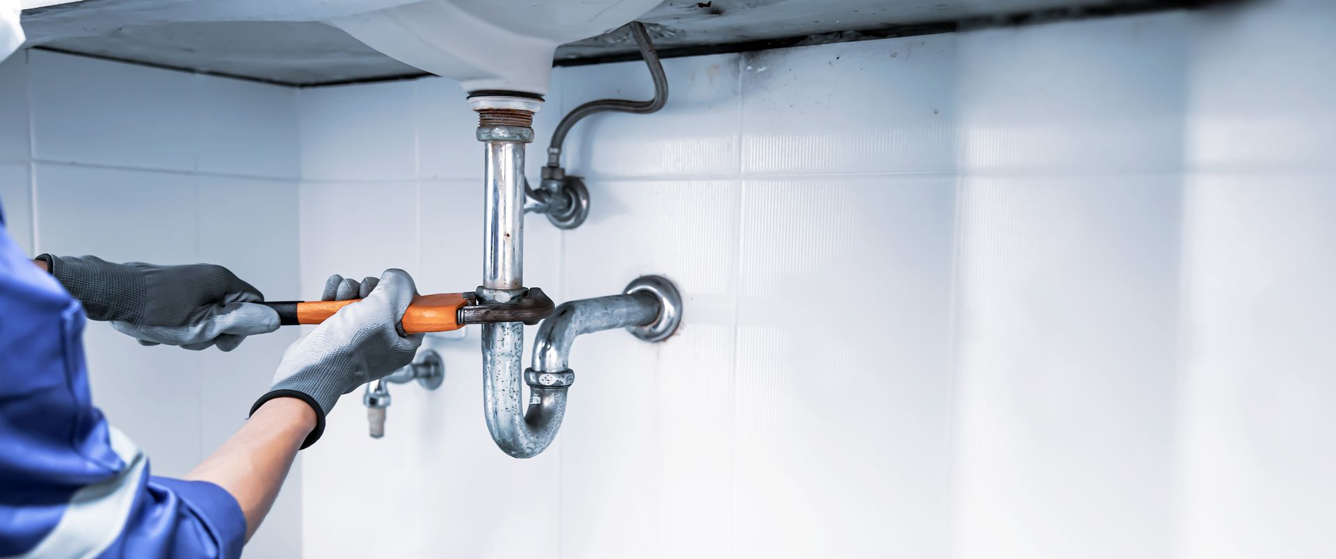 Un plombier tient une pince pour réparer le siphon d'un lavabo.