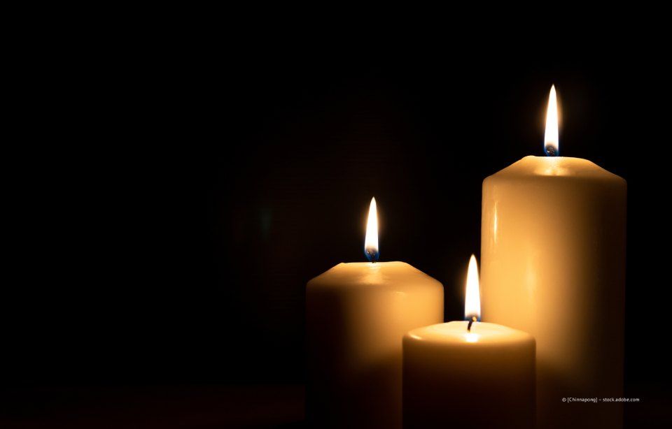 Drei sanft leuchtende weiße Kerzen vor dunklem Hintergrund.
