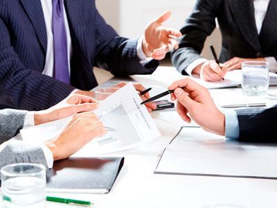 Hombres de negocios con traje revisando documentos alrededor de una mesa.