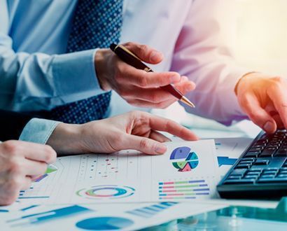 Dos personas analizando informes financieros con una calculadora y un bolígrafo en un escritorio.