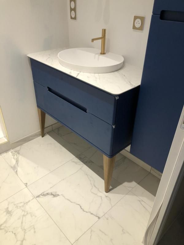 Pose de carrelage blanc dans une salle de bains aux meubles bleus