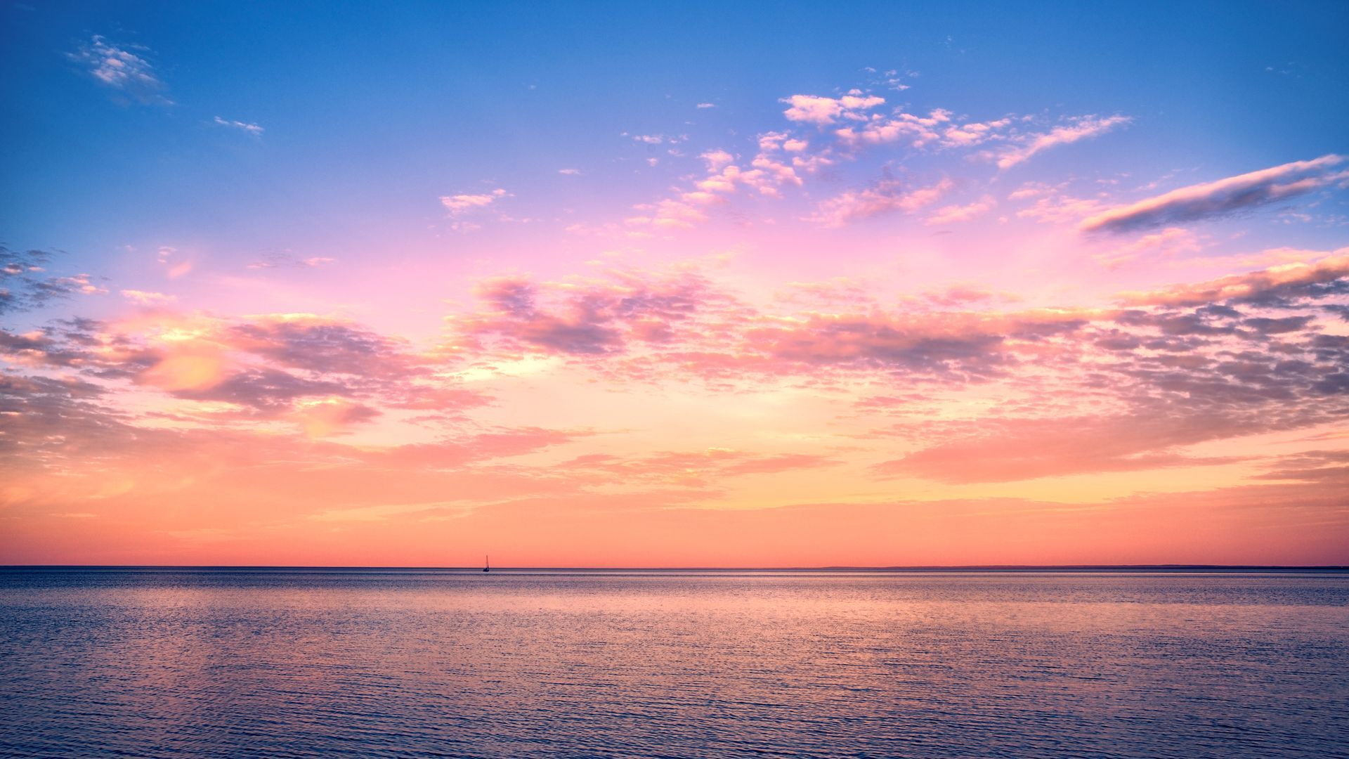 Coucher de soleil rose et orange sur un océan calme parsemé de nuages ​​épars
