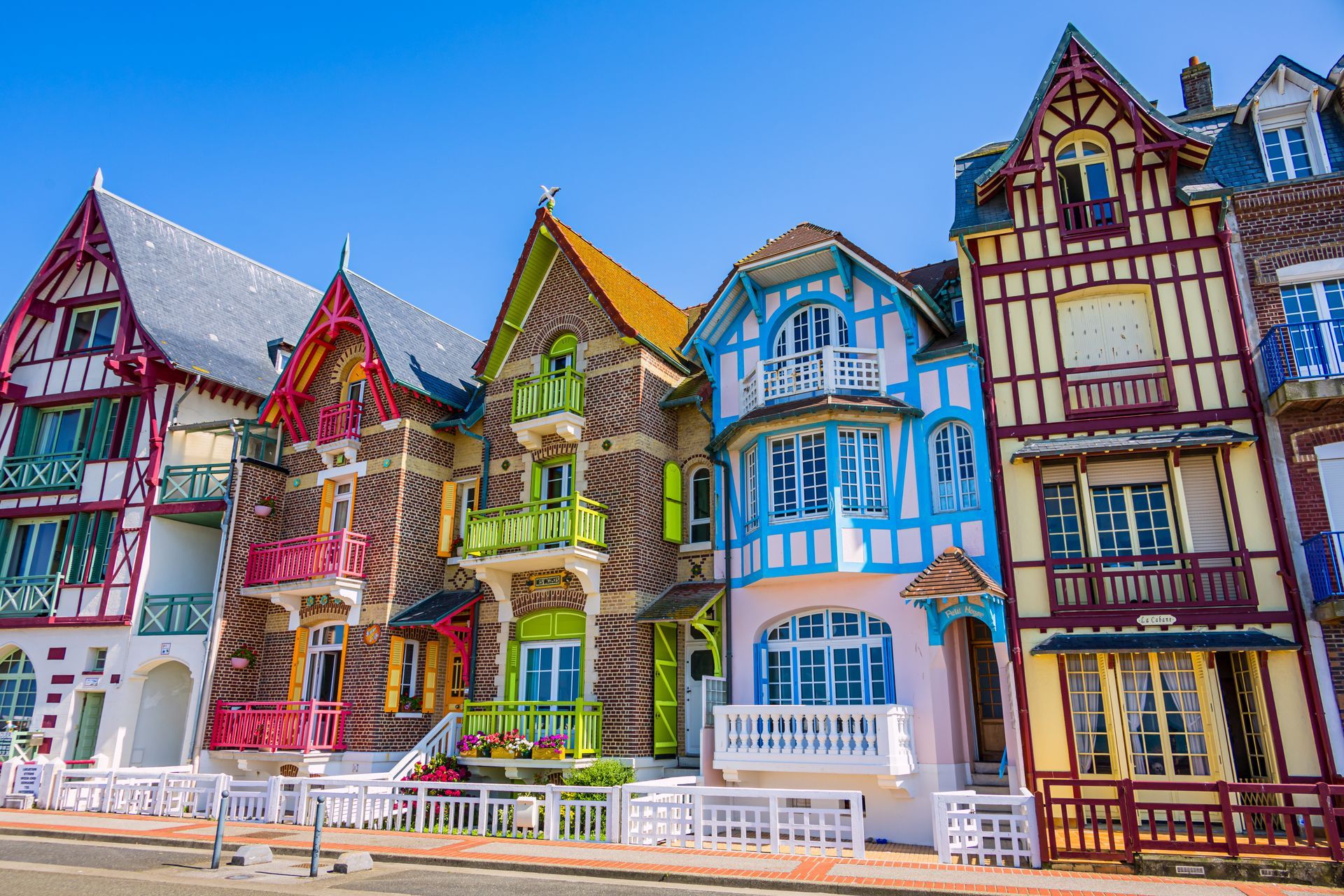 Rangée colorée de maisons à colombages ornées, aux façades rouges, bleues et jaunes, dans une rue ensoleillée