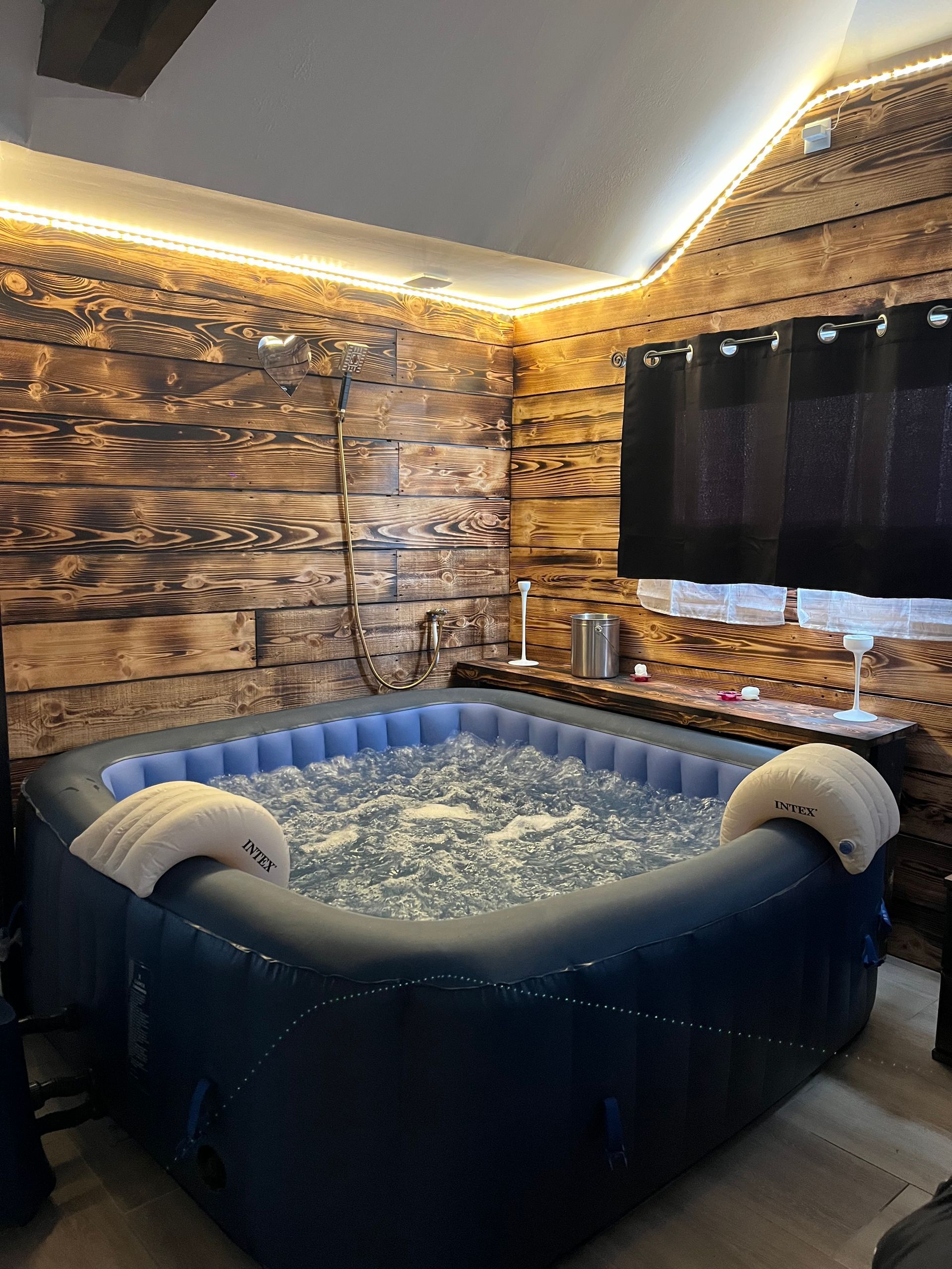 Cabine confortable avec jacuzzi gonflable bleu, murs lambrissés et guirlandes lumineuses chaleureuses.