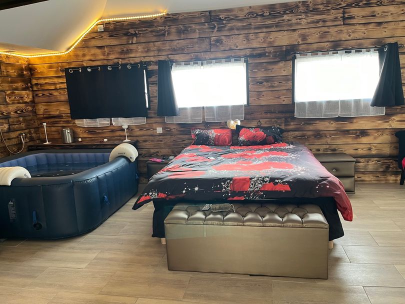 Chambre confortable avec murs en pierre, fenêtres noires, lit avec couverture rouge et canapé bleu foncé.