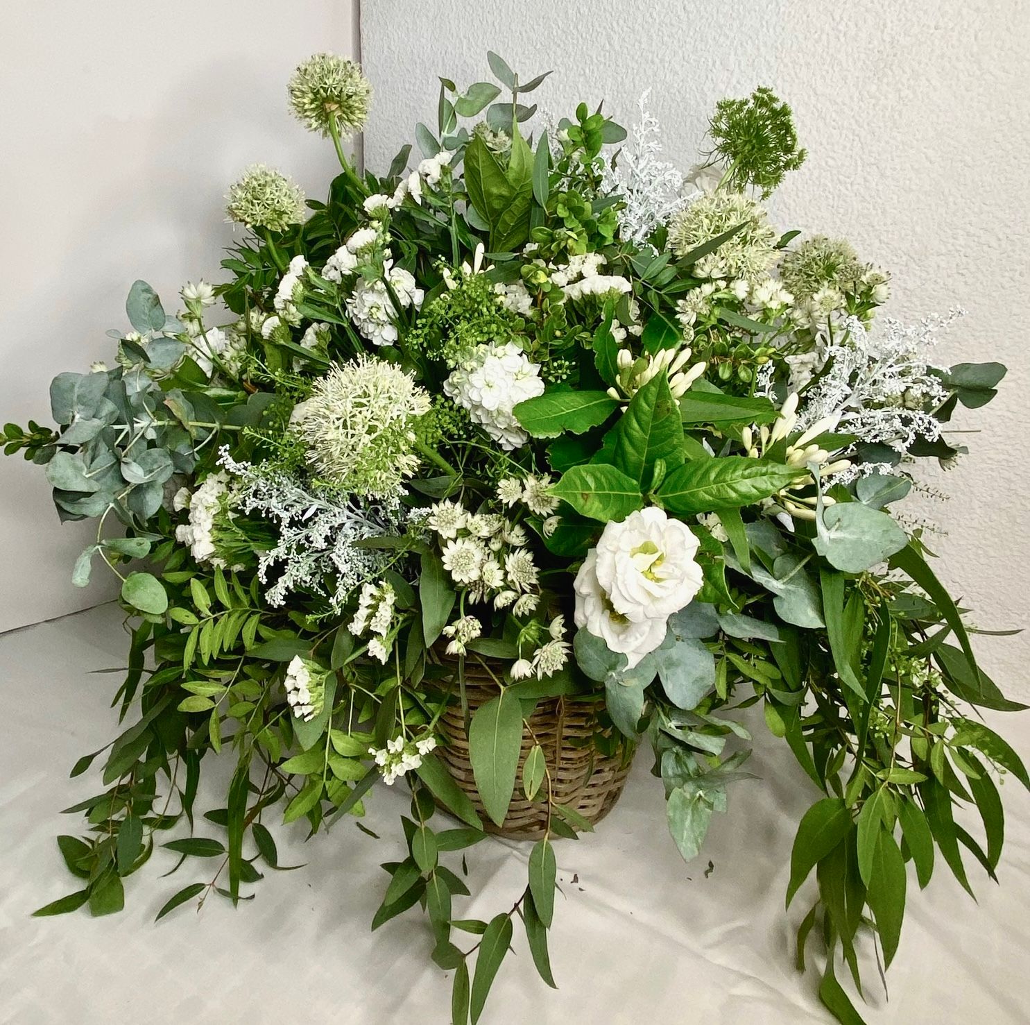 Una cesta llena de flores blancas y vegetación se encuentra sobre una mesa.