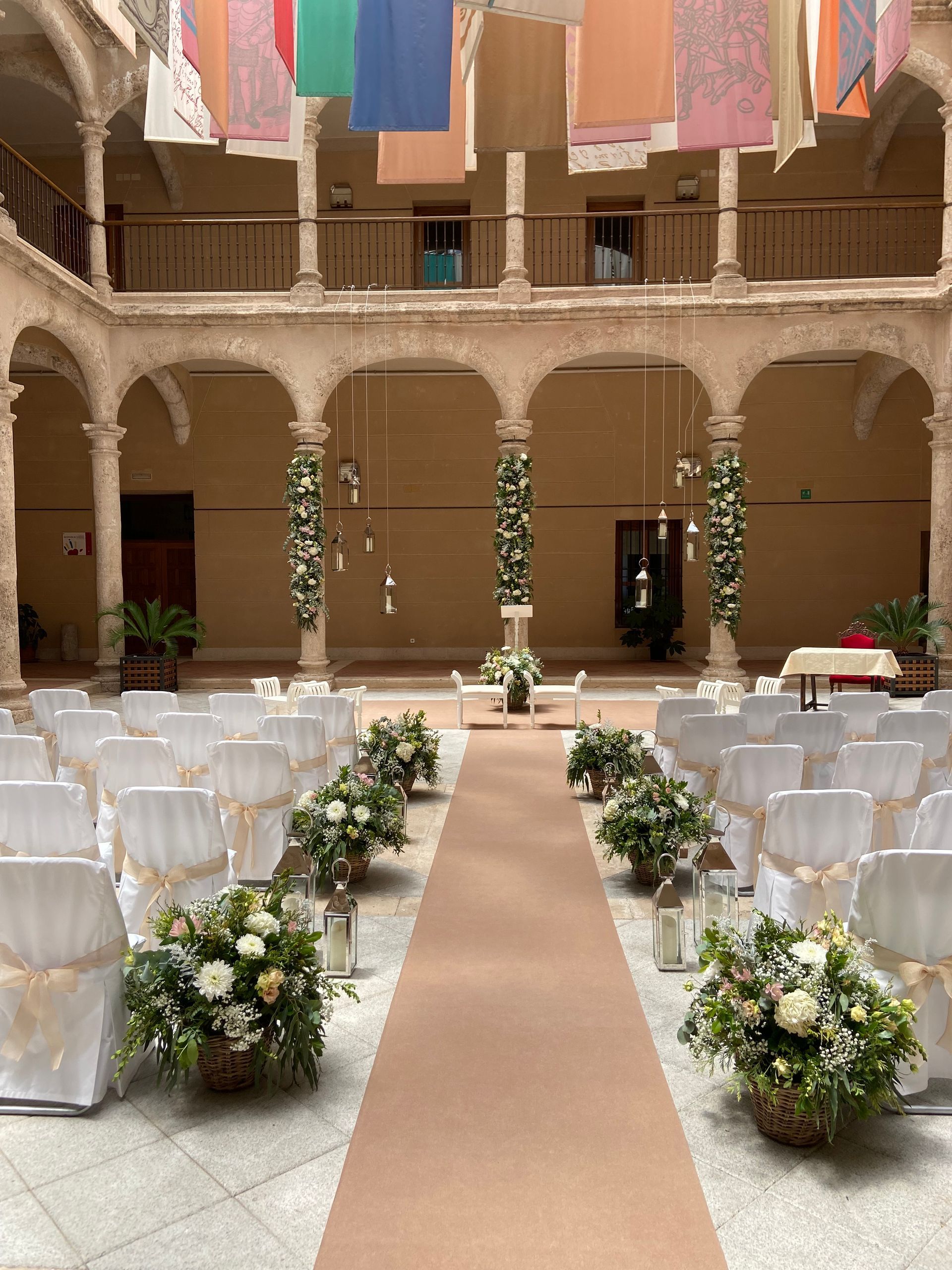 Se organiza una ceremonia de boda en un patio con sillas blancas y flores.