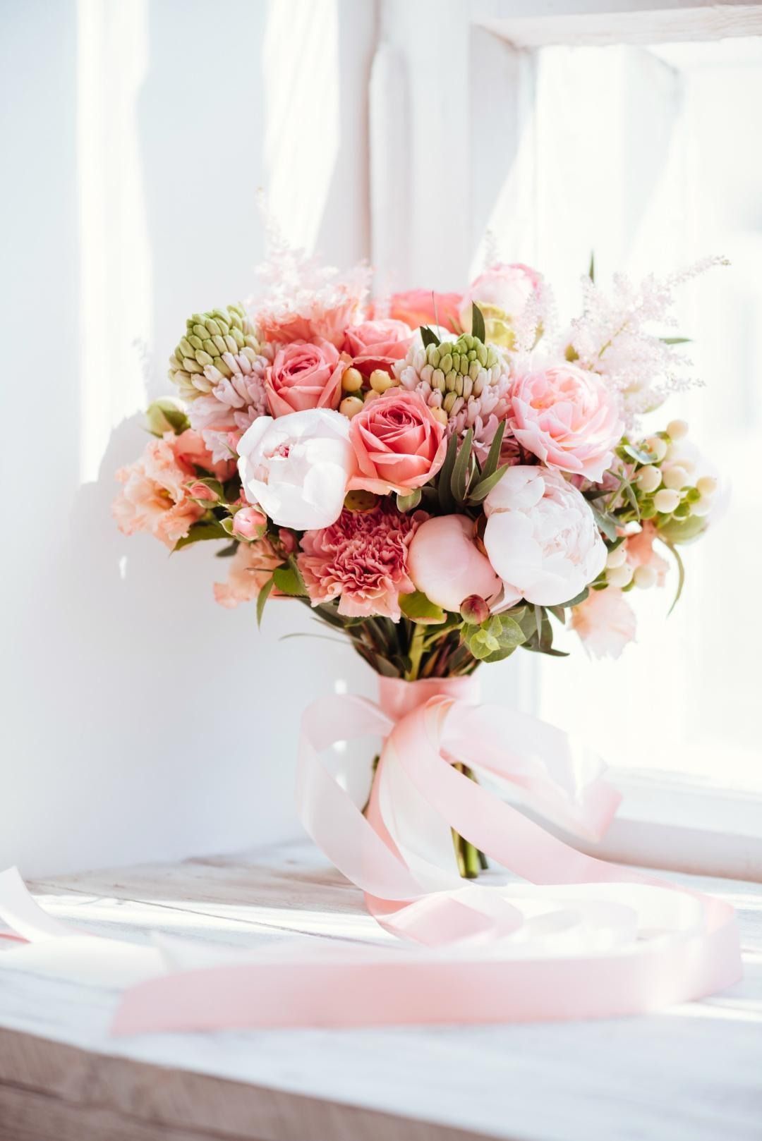 Un ramo de flores rosas está sentado en el alféizar de una ventana.