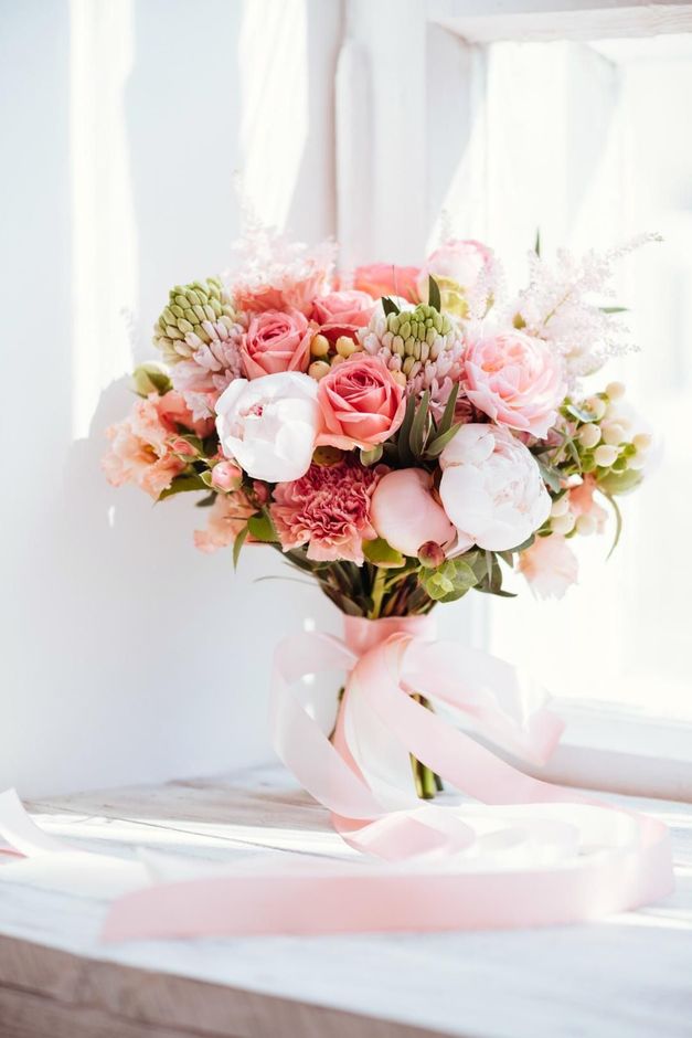 Un ramo de flores rosas está sentado en el alféizar de una ventana.