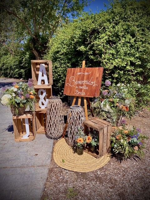 Un cartel de madera que dice bienvenidos está rodeado de cajas de madera y flores.
