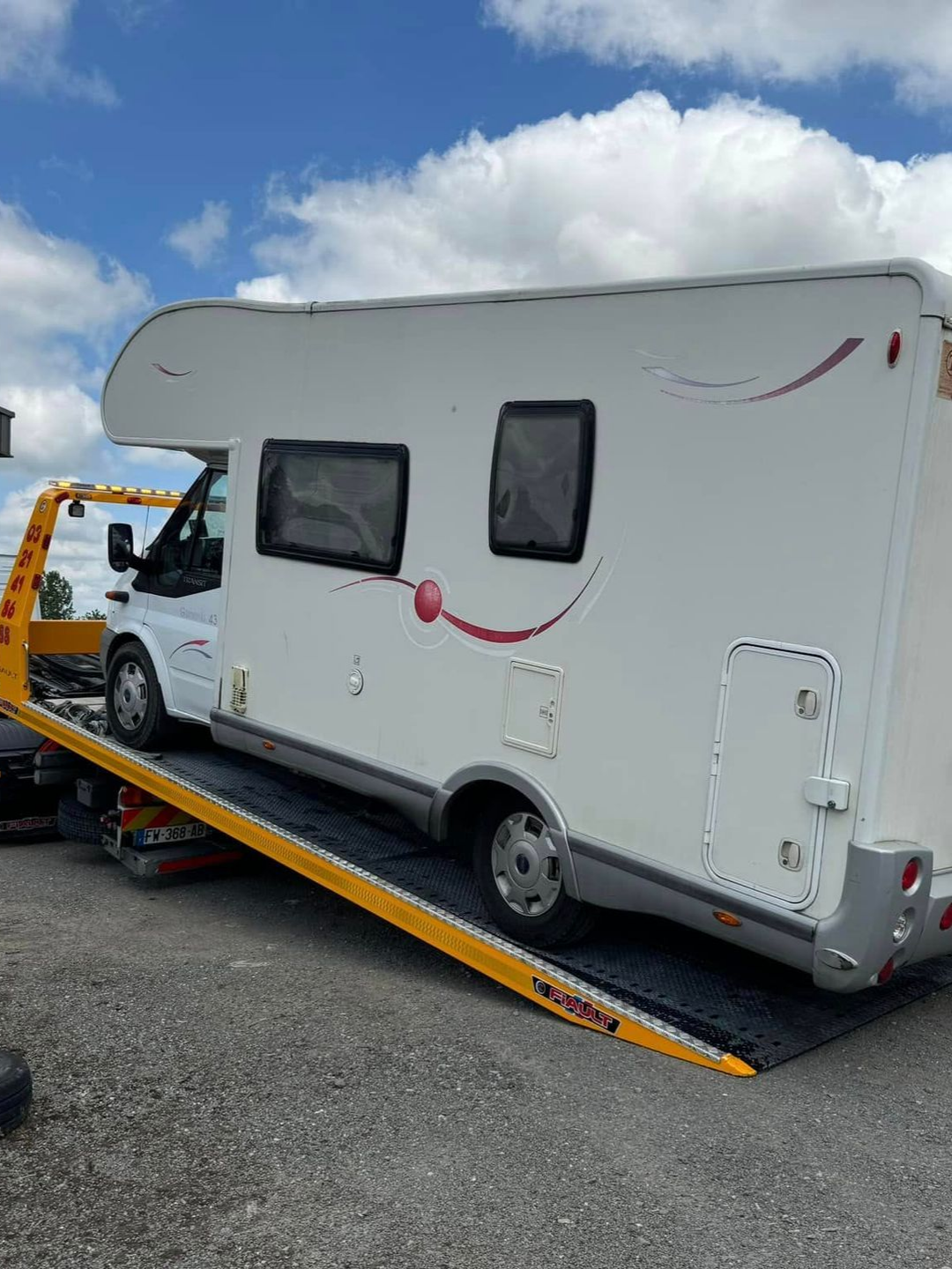 Un camping-car blanc est chargé sur une dépanneuse jaune par une journée ensoleillée.