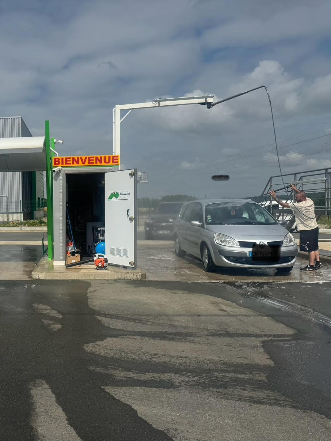 Voiture lavée dans une station de lavage automatique sous un ciel nuageux.