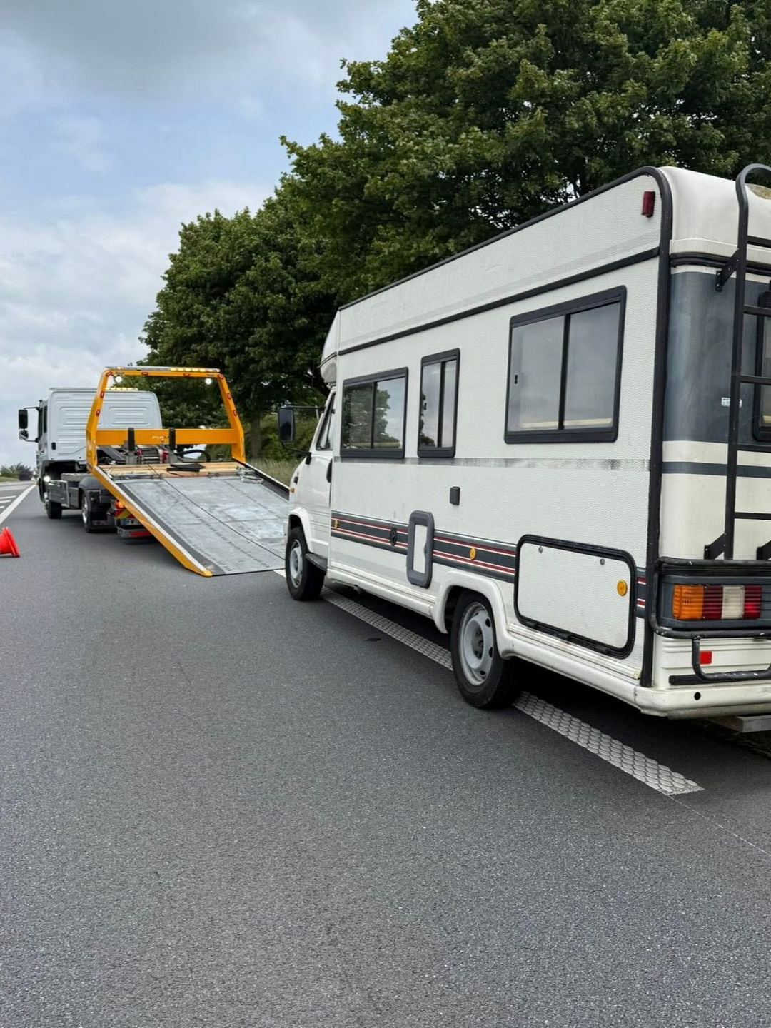Un camping-car blanc est chargé sur une dépanneuse à plateau sur une autoroute.