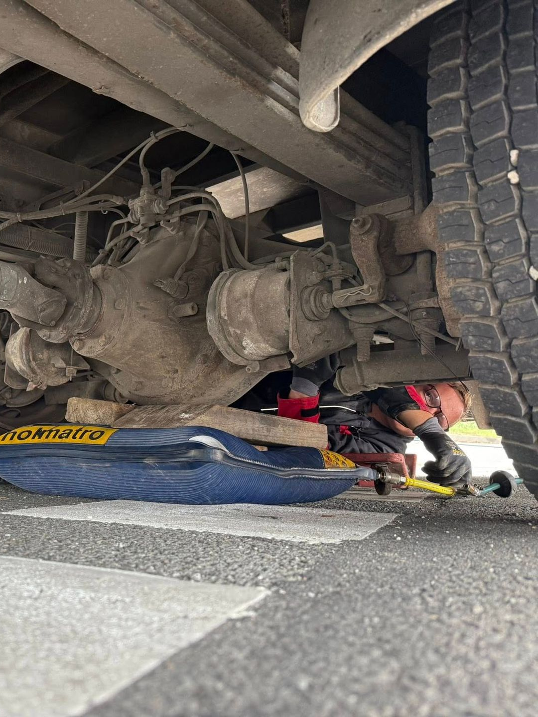 Un mécanicien travaille sous un camion, à l'aide d'outils. Le camion est soulevé par un cric.
