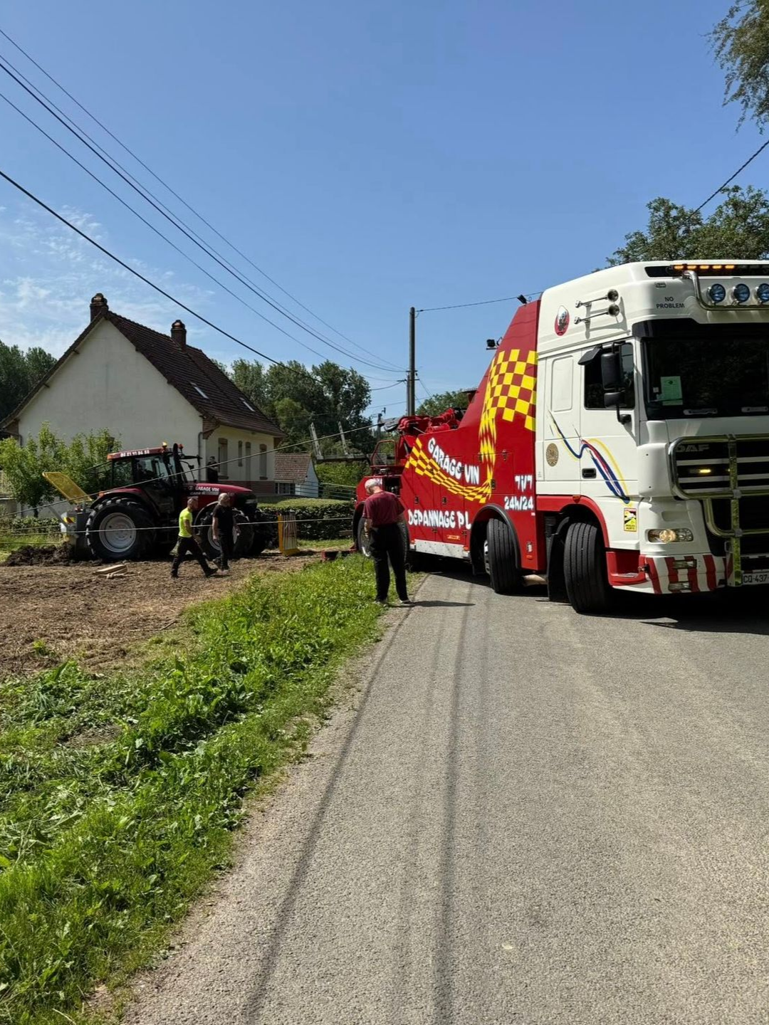 Dépanneuse en bord de route, tracteur dégagé d'un champ, maison en arrière-plan.