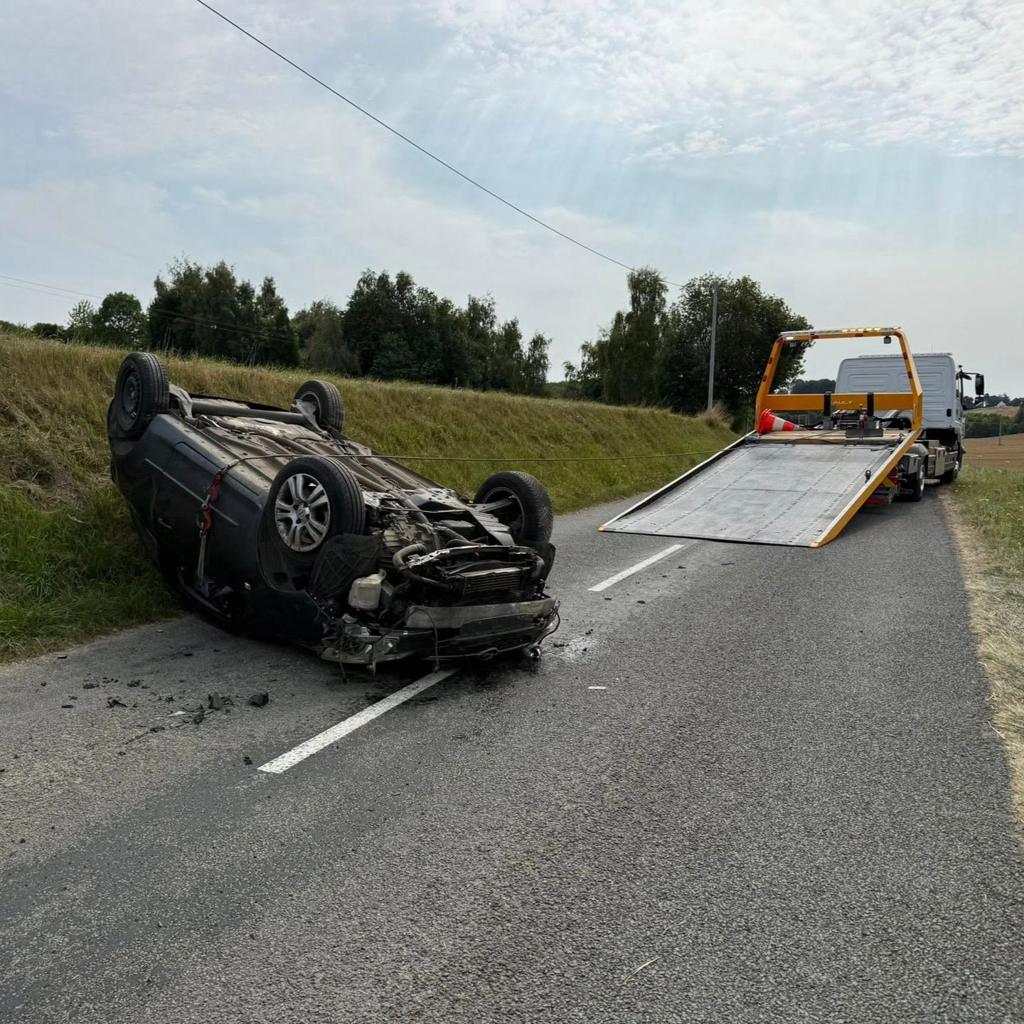 Une voiture noire s'est renversée sur la route, une dépanneuse s'approche.