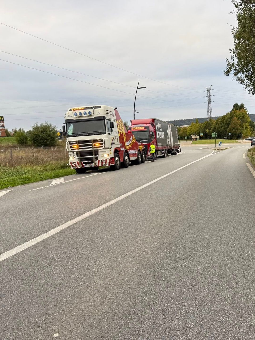 Une dépanneuse tire une grosse remorque sur une route. Ciel couvert.