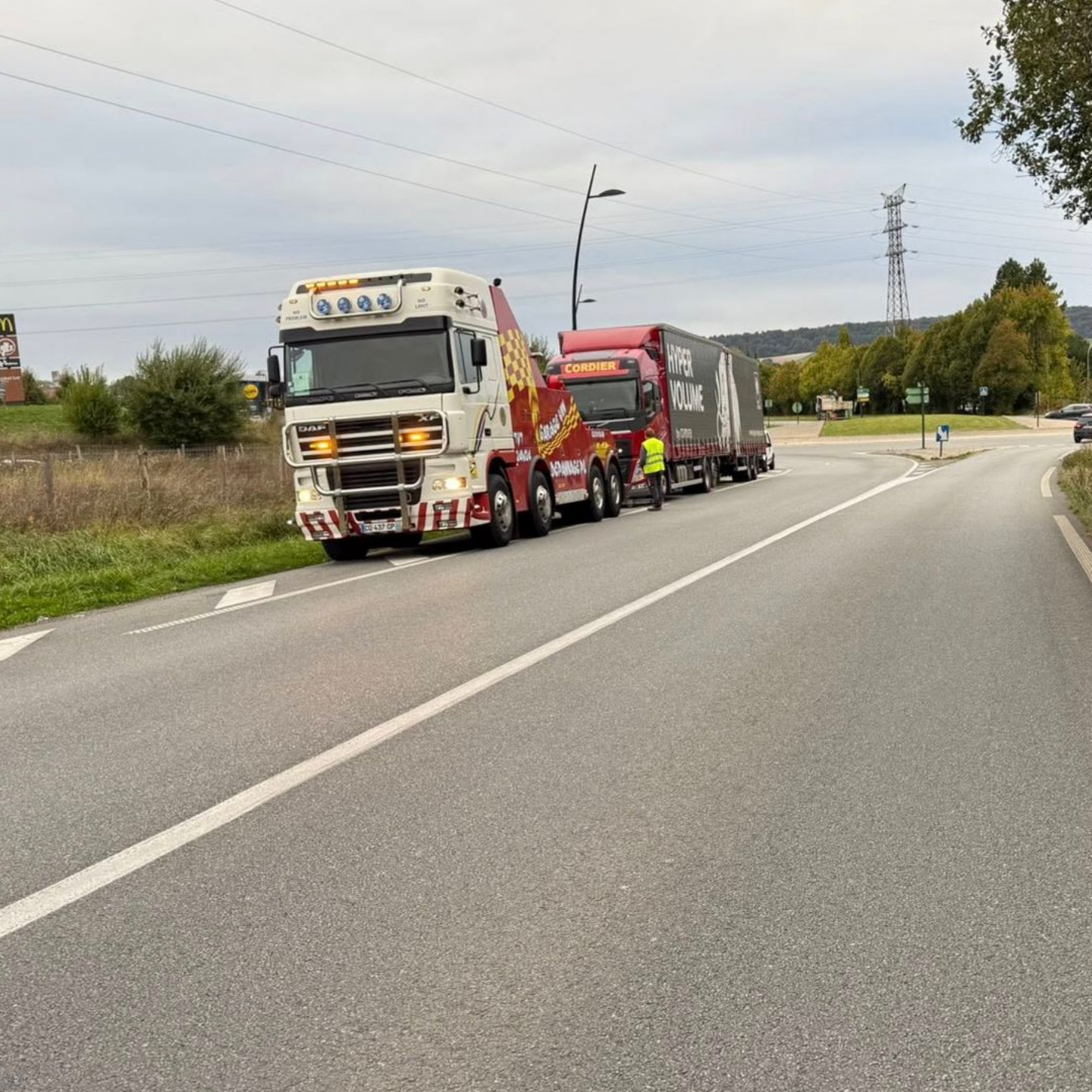 Une dépanneuse blanche transporte un poids lourds sur une route goudronnée, avec des arbres en arrière-plan.