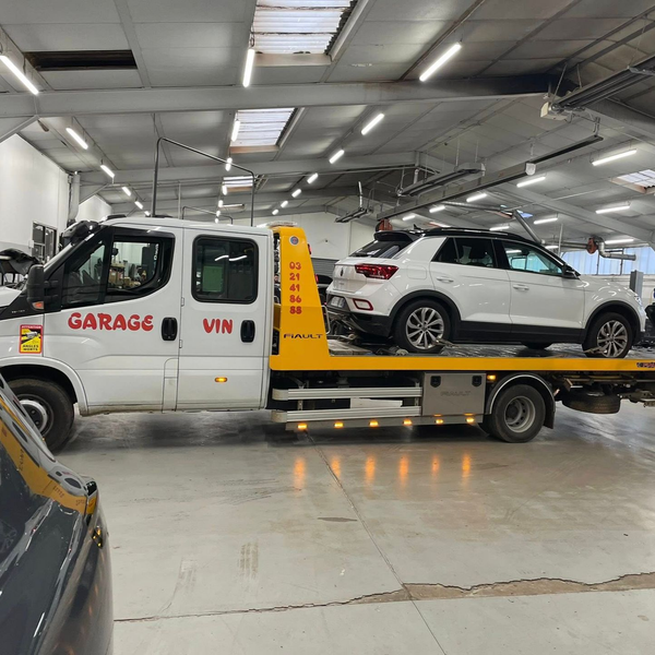 Une dépanneuse dans un garage transporte un SUV blanc. Le numéro VIN de la dépanneuse est inscrit dessus.